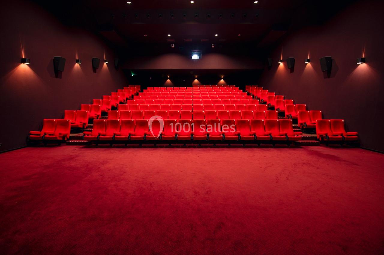 Salle de cinéma vide avec des rangées de fauteuils rouges et un éclairage tamisé.