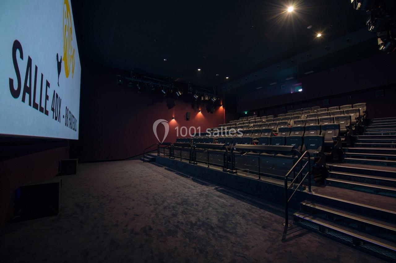 Salle de cinéma vide avec rangées de sièges, écran allumé à gauche et éclairage tamisé.