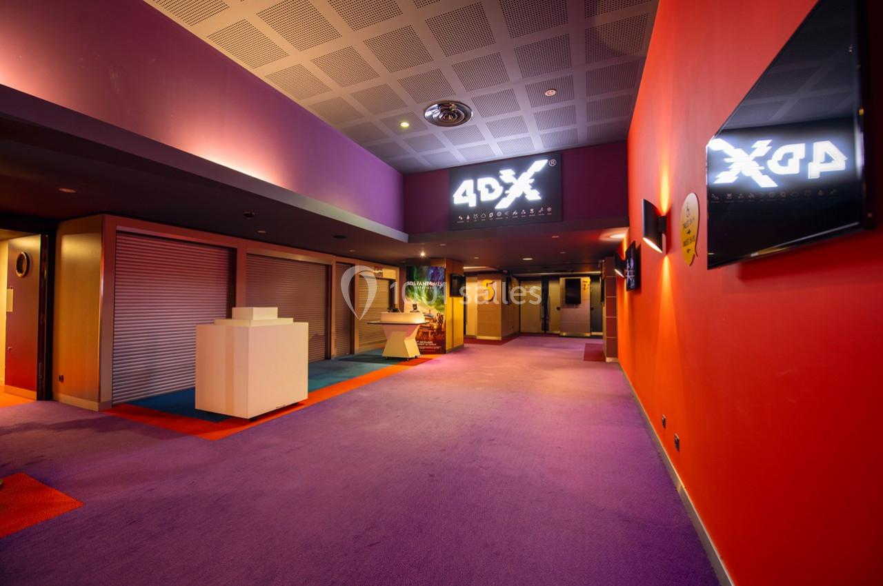 Couloir d'un cinéma avec moquette violette, murs colorés, enseigne ’4DX’ lumineuse et accès aux salles numérotées.