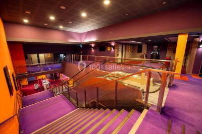 Espace intérieur spacieux avec moquette rouge, colonnes, éclairage tamisé et fauteuils disposés près des vitrines.