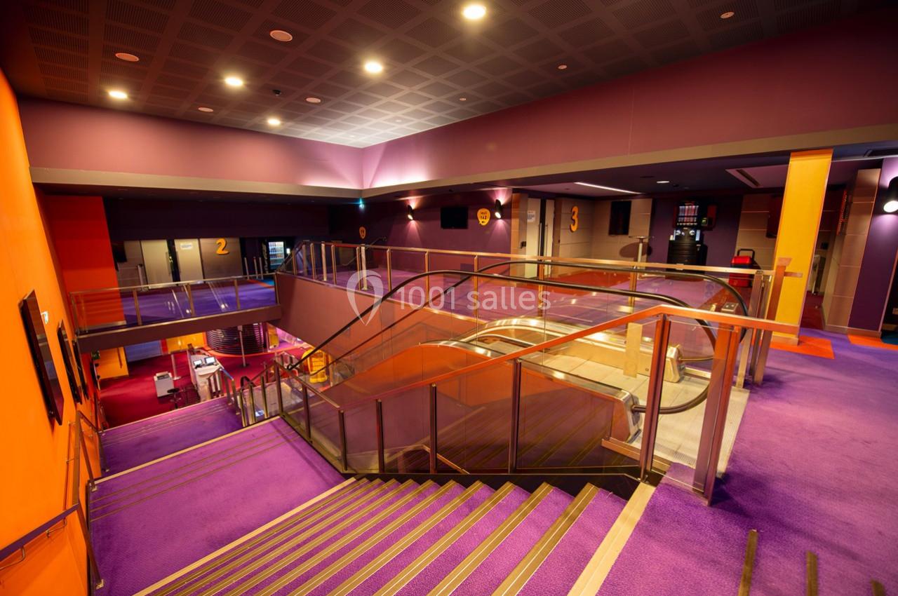 Escalier et escalators dans un intérieur moderne aux murs violets et orange, éclairé par des lumières au plafond.