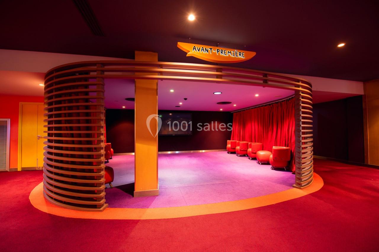 Espace lounge avec fauteuils rouges et éclairage tamisé, situé sous une enseigne ’Avant-Première’.