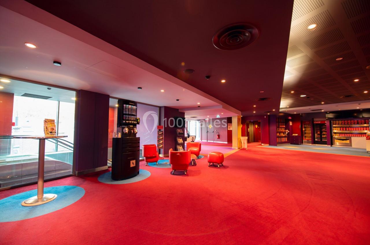 Hall spacieux avec moquette rouge, fauteuils, distributeurs automatiques et étagères de produits en arrière-plan.