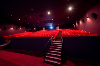 Rangée de fauteuils rouges numérotés dans une salle de cinéma sombre.