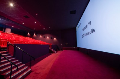 Rangée de fauteuils rouges numérotés dans une salle de cinéma sombre.