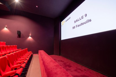 Rangée de fauteuils rouges numérotés dans une salle de cinéma sombre.