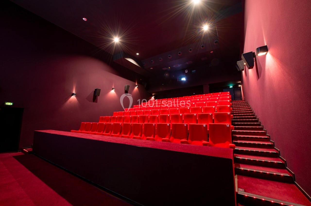 Salle de cinéma vide avec des rangées de sièges rouges et un éclairage tamisé.