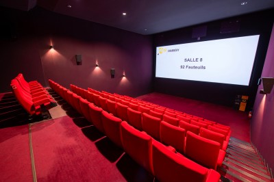 Rangée de fauteuils rouges numérotés dans une salle de cinéma sombre.