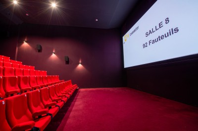 Rangée de fauteuils rouges numérotés dans une salle de cinéma sombre.