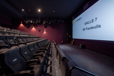 Rangée de fauteuils rouges numérotés dans une salle de cinéma sombre.