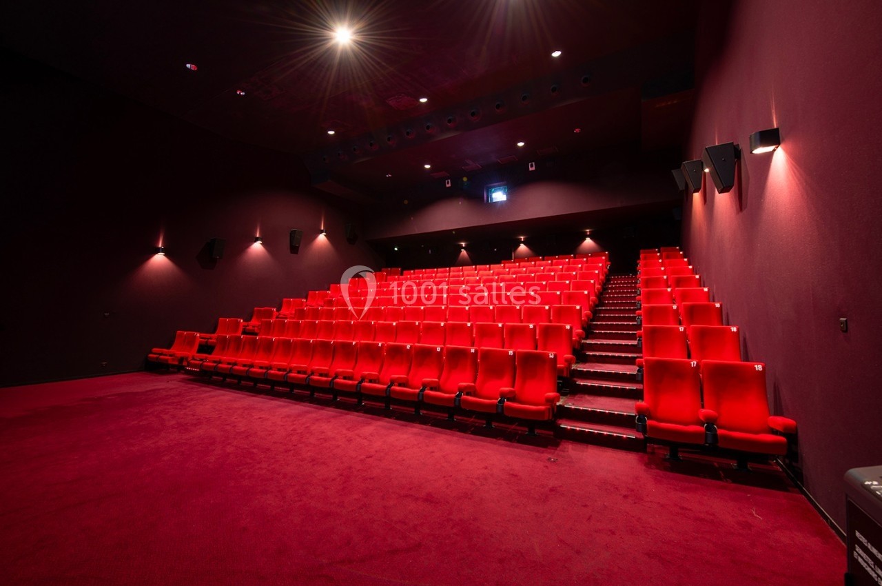 Salle de cinéma vide avec des rangées de sièges rouges et un éclairage tamisé.