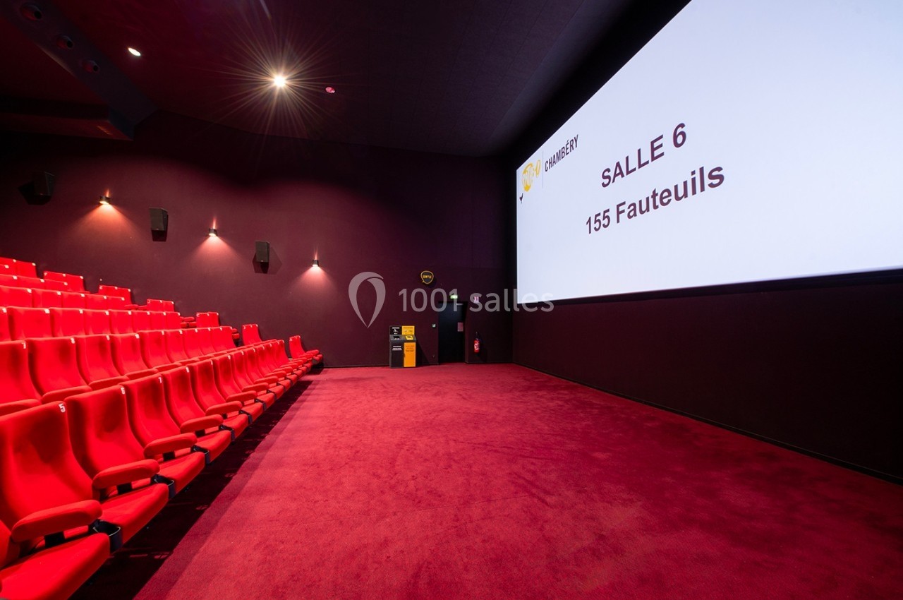 Salle de cinéma vide avec des fauteuils rouges, un écran affichant ’Salle 6 - 155 Fauteuils’ et un éclairage tamisé.
