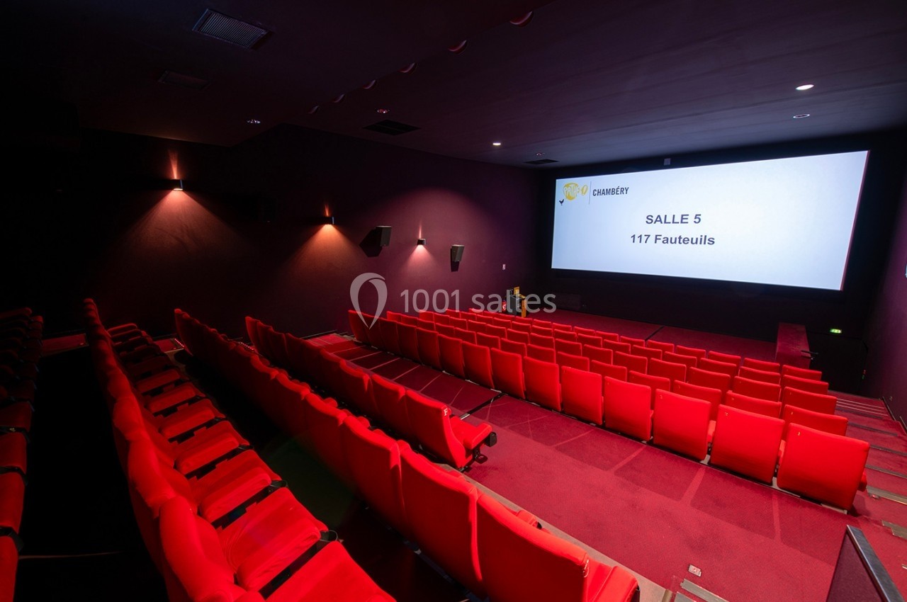 Salle de cinéma vide avec des rangées de fauteuils rouges et un écran affichant ’Salle 5 - 117 Fauteuils’.
