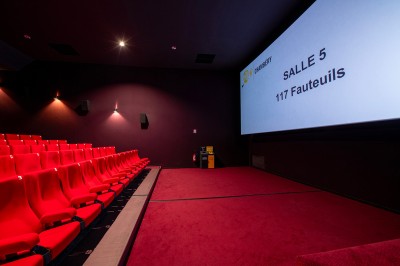 Rangée de fauteuils rouges numérotés dans une salle de cinéma sombre.