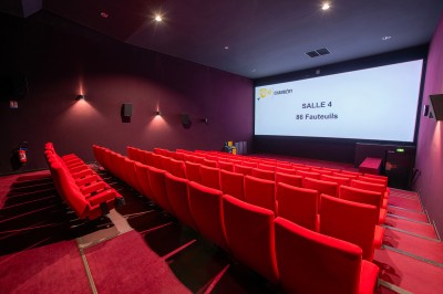 Rangée de fauteuils rouges numérotés dans une salle de cinéma sombre.