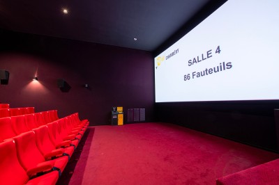 Rangée de fauteuils rouges numérotés dans une salle de cinéma sombre.