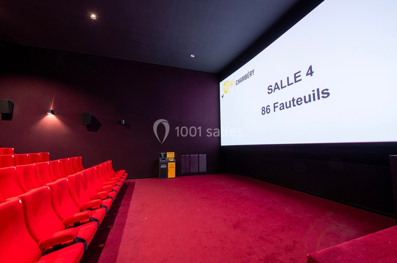 Salle de cinéma avec des sièges rouges, un écran affichant ’Salle 4, 86 fauteuils’ et un mur sombre.