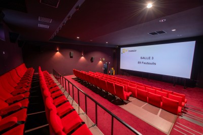 Rangée de fauteuils rouges numérotés dans une salle de cinéma sombre.