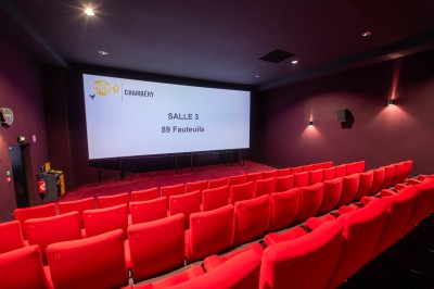 Rangée de fauteuils rouges numérotés dans une salle de cinéma sombre.