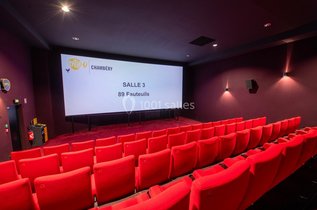 Salle de cinéma vide avec des rangées de fauteuils rouges, écran affichant ’Salle 3 - 89 Fauteuils’.