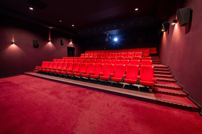 Rangée de fauteuils rouges numérotés dans une salle de cinéma sombre.