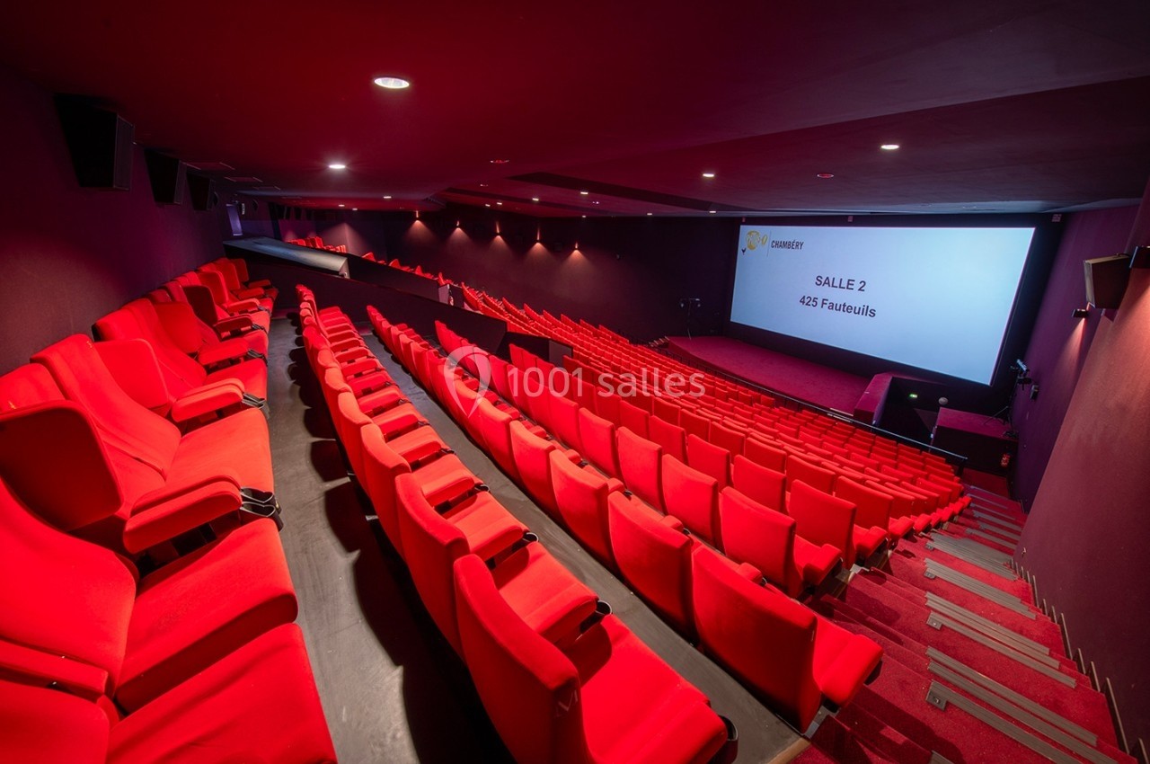Salle de cinéma moderne avec des sièges rouges, un écran affichant ’Salle 2 - 425 fauteuils’ et un éclairage tamisé.