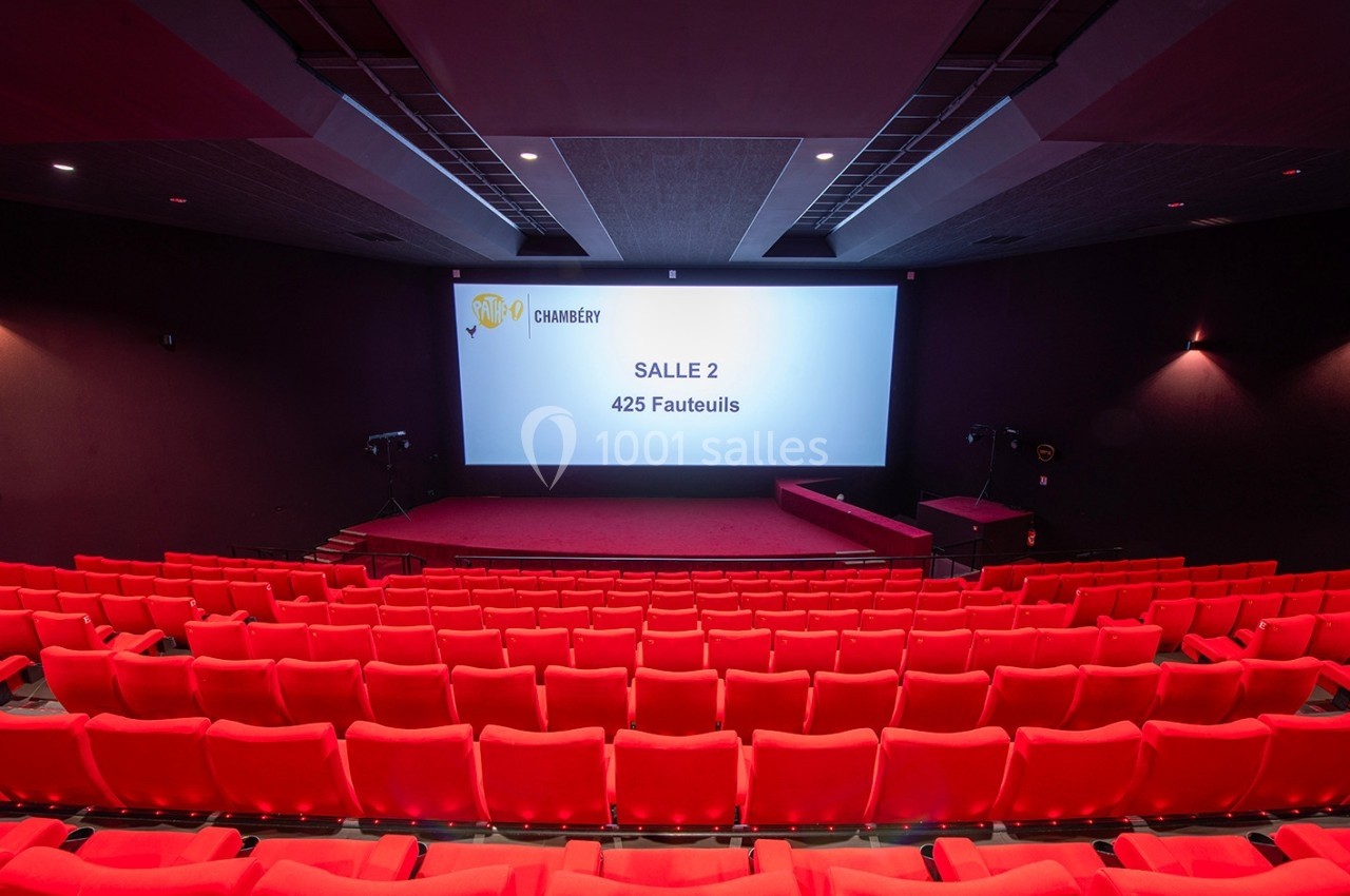 Salle de cinéma avec 425 fauteuils rouges, écran blanc affichant ’Salle 2’ et éclairage tamisé.