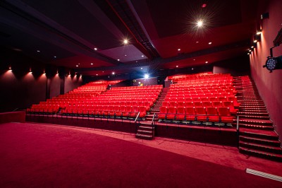 Rangée de fauteuils rouges numérotés dans une salle de cinéma sombre.