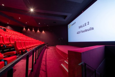 Rangée de fauteuils rouges numérotés dans une salle de cinéma sombre.