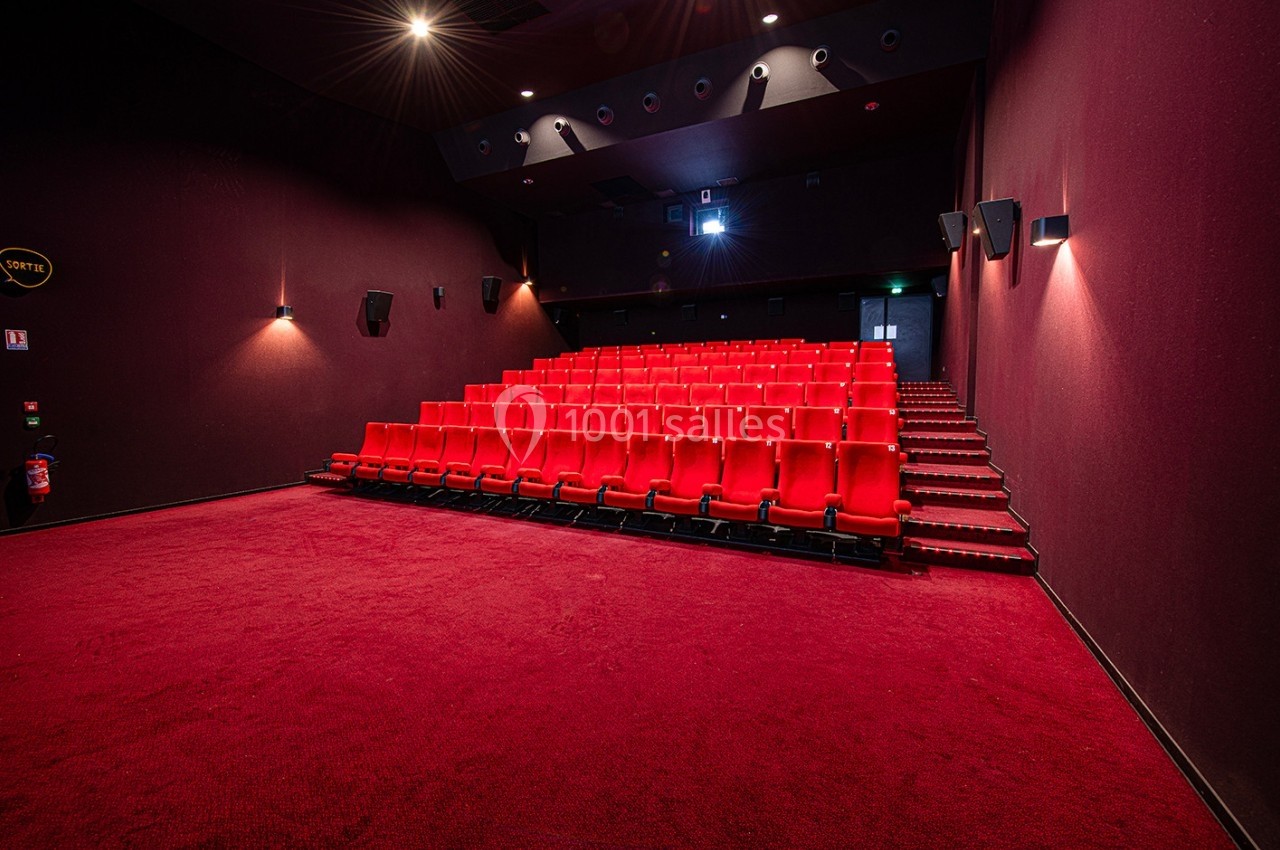 Salle de cinéma vide avec rangées de sièges rouges, éclairage tamisé et moquette rouge au sol.