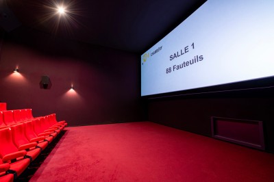 Rangée de fauteuils rouges numérotés dans une salle de cinéma sombre.