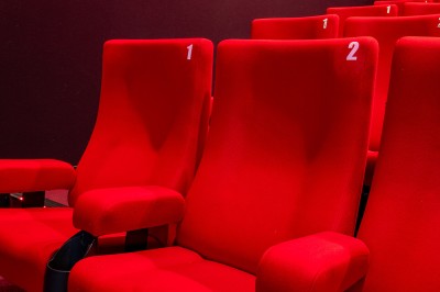 Rangée de fauteuils rouges numérotés dans une salle de cinéma sombre.