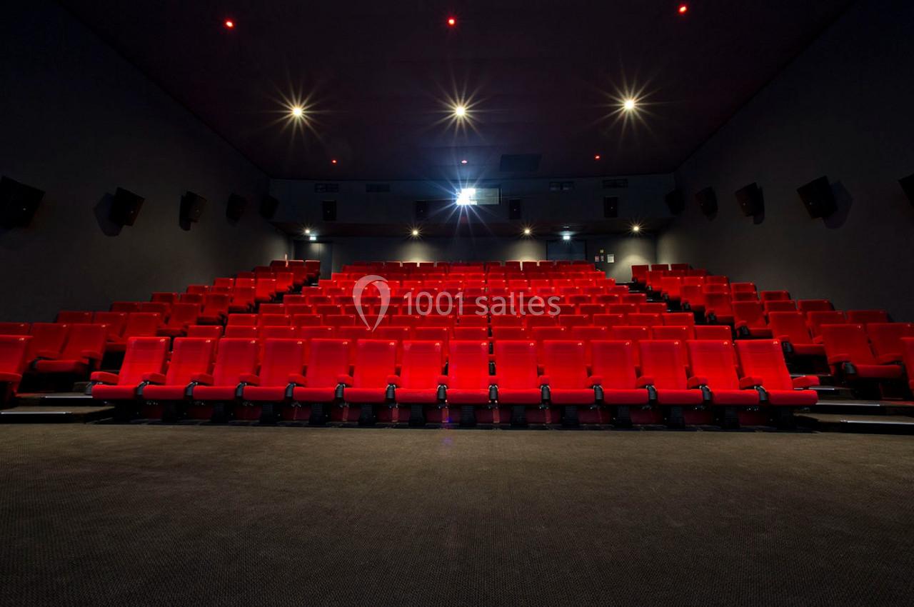 Salle de cinéma vide avec des rangées de sièges rouges et un écran blanc éclairé à l'arrière-plan.