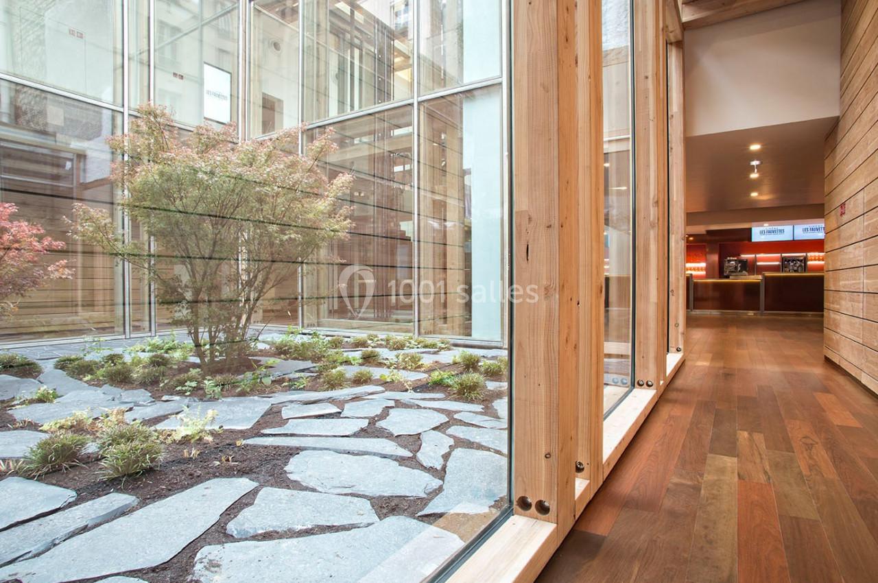 Vue d'un jardin intérieur avec des pierres et des plantes, entouré de grandes baies vitrées et d'un sol en bois.