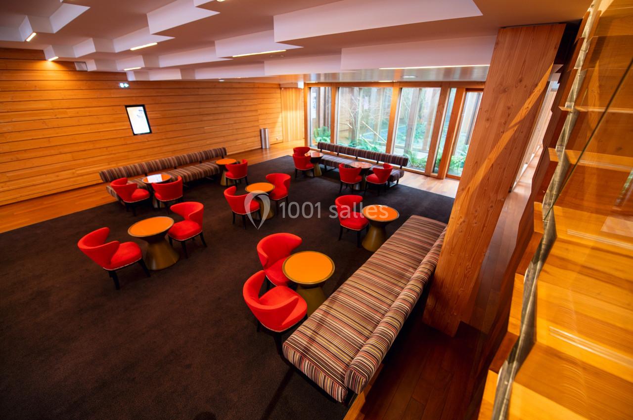 Salle lumineuse avec tables rondes, chaises rouges et banquettes rayées, parquet en bois et grandes baies vitrées.