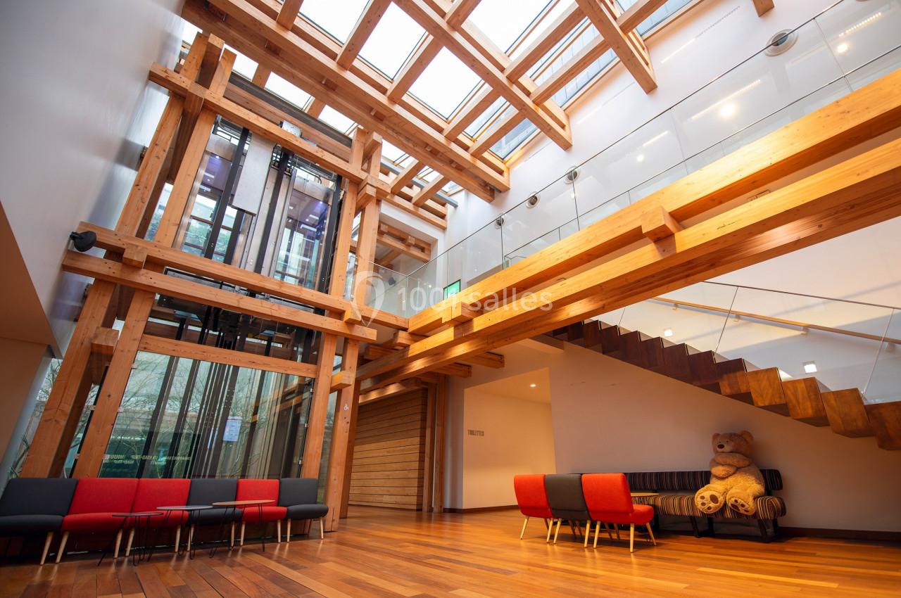 Intérieur lumineux avec structure en bois, escalier moderne, sièges colorés et un grand ours en peluche.