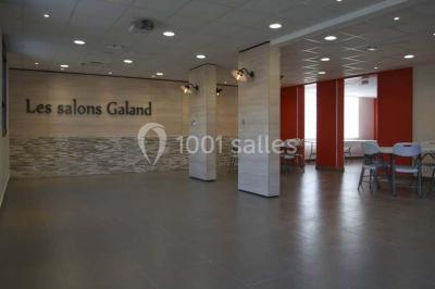 Un petit pont en bois traverse un bassin entouré de végétation, avec une route et des bâtiments en arrière-plan.