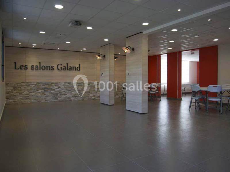 Salle lumineuse avec murs en pierre et panneaux rouges, équipée de chaises et tables pliantes.