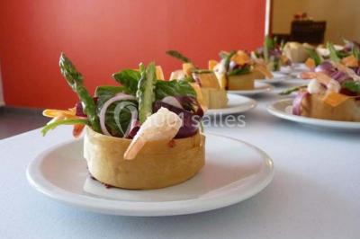 Un petit pont en bois traverse un bassin entouré de végétation, avec une route et des bâtiments en arrière-plan.