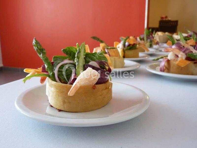 Assiette contenant une tartelette garnie de crevettes, asperges, légumes frais et feuilles de salade.