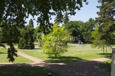 Un petit pont en bois traverse un bassin entouré de végétation, avec une route et des bâtiments en arrière-plan.
