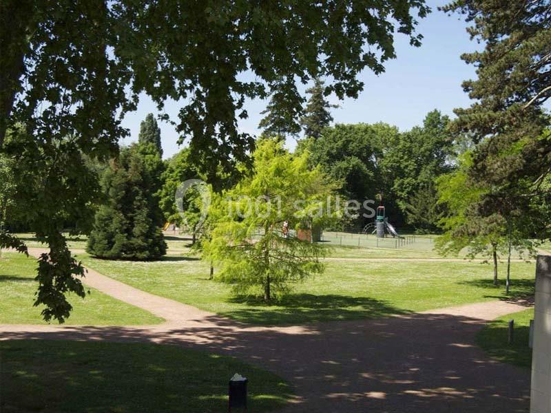 Allée bordée d'arbres dans un parc verdoyant avec une aire de jeux visible en arrière-plan.