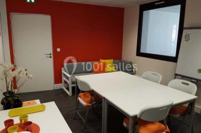 Un petit pont en bois traverse un bassin entouré de végétation, avec une route et des bâtiments en arrière-plan.