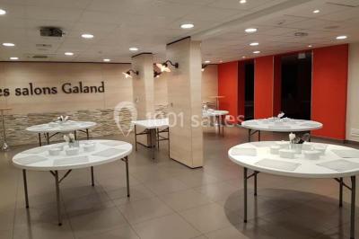 Un petit pont en bois traverse un bassin entouré de végétation, avec une route et des bâtiments en arrière-plan.