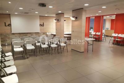 Un petit pont en bois traverse un bassin entouré de végétation, avec une route et des bâtiments en arrière-plan.