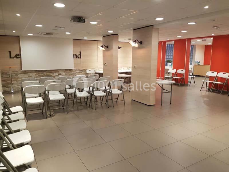 Salle de réunion avec chaises pliantes alignées, écran de projection et murs clairs ornés de pierres et de panneaux rouges.