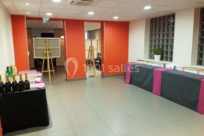 Un petit pont en bois traverse un bassin entouré de végétation, avec une route et des bâtiments en arrière-plan.