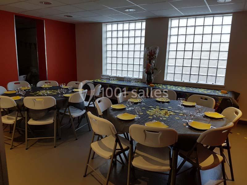 Salle décorée avec des tables rondes et rectangulaires dressées pour un repas, avec assiettes et verres.