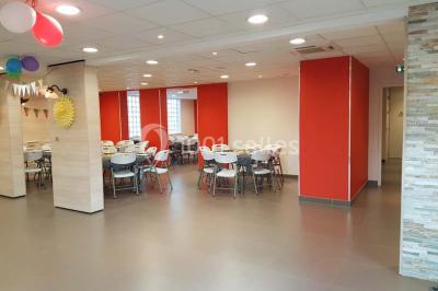 Un petit pont en bois traverse un bassin entouré de végétation, avec une route et des bâtiments en arrière-plan.