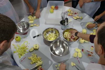 Un petit pont en bois traverse un bassin entouré de végétation, avec une route et des bâtiments en arrière-plan.